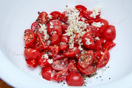 Добавляем соль, перец оливковое масло к помидорам и чесноку для радужной форели с травами и томатами в конверте