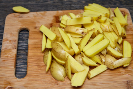 700 грам картоплі промийте та поріжте на невеликі довгі скибочки. Перекладіть у велику миску, приправте щіпкою солі і щедрою порцією свіжомеленого чорного перцю, полийте олією і перемішайте.