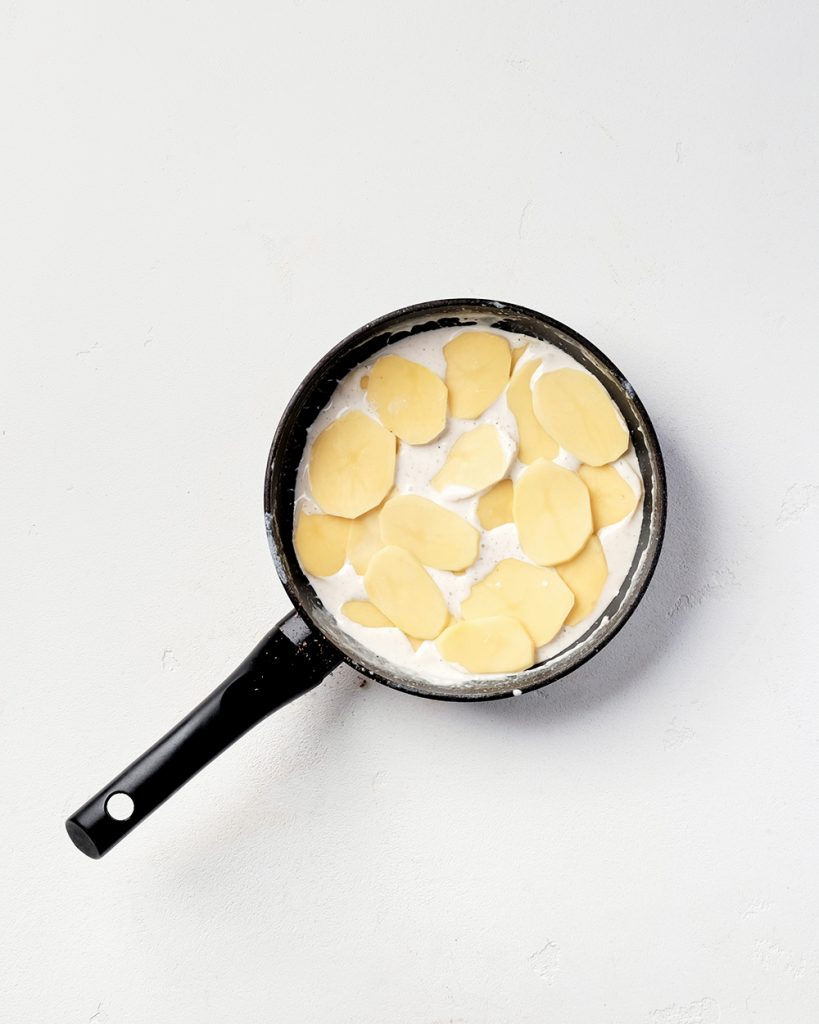 Зніміть сковороду з вогню і приправте вершки щіпкою солі, щіпкою перцю та свіжонатертим мускатним горіхом (приблизно 1/4 чайної ложки). Перемішайте. Перекладіть картоплю в сковороду (залишіть трохи, щоб гарно викласти верхній шар), рівномірно розподіліть.