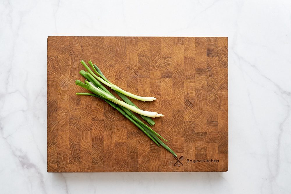 Стебли зеленого лука на разделочной кухонной доске