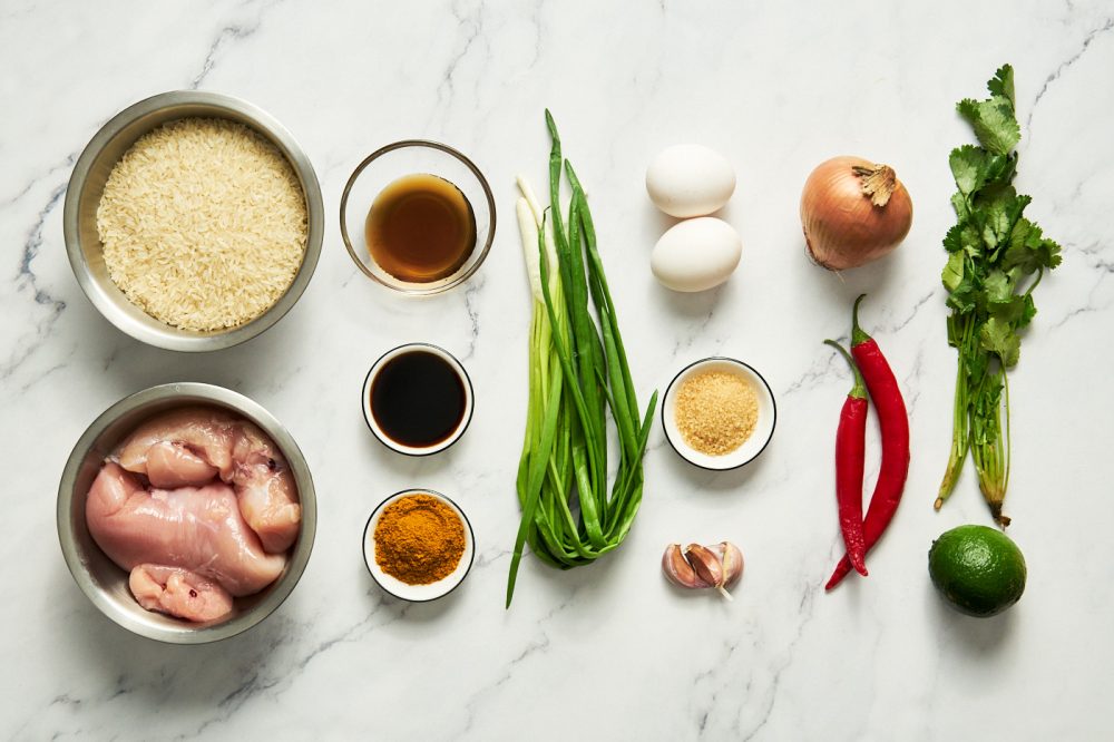 Ingredients for Thai style fried rice with chicken and curry: chicken fillet, salt, fish sauce, soy sauce, rice, eggs, garlic, onion, curry powder, green Thai chili, shallots, coriander sprigs, vegetable oil.
