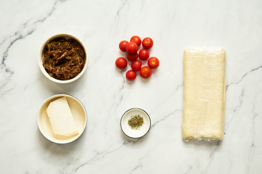 Ингредиенты необходимые для приготовления татрта: слоеное тесто, томаты черри, карамелизированный лук, тимьян (листьев свежего или столько же сушеного), козий сыр