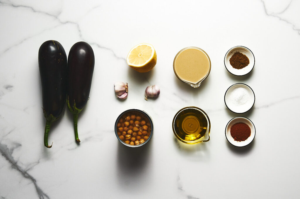 Ингредиенты необходимые для приготовления баклажанового хумуса: тахини, отварной нут, чеснок, оливковое масло, лимонная цедра и сок, мякоть печёного баклажана, копчёная паприка, соль, молотая зира
