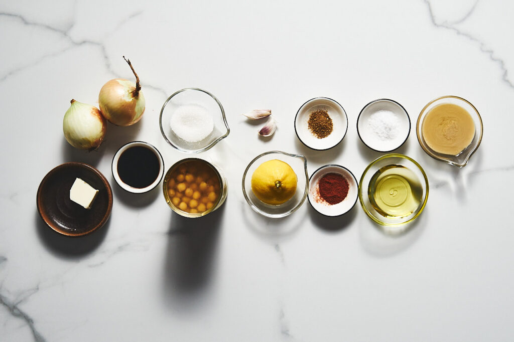Ингредиенты необходимые для приготовления Хумуса с карамелизированным луком и бальзамическим уксусом: лук, сливочное масло, тахини, чеснок, оливковое масло, бальзамический уксус, сахар, нут, лимон, соль, зира, паприка