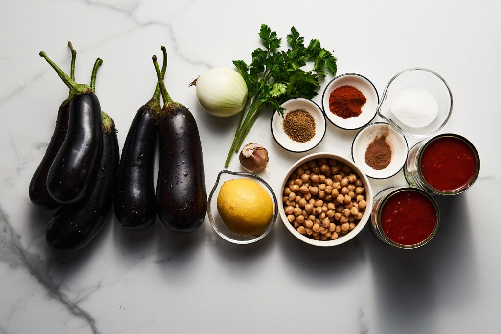Ingredients needed for Lebanese moussaka: eggplant, canned chickpeas, onion, garlic, tomatoes in their own juice, zira, paprika, cinnamon, sugar, olive oil, parsley, lemon